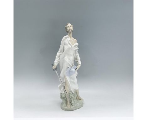 Glazed porcelain figure of Don Quixote standing in a white nightshirt holding a sword in one hand and his blue hat in the oth
