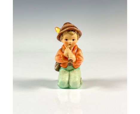 A matte figure of a boy wearing an orange coat, green pants, and a brown hat as he is playing the flute. M.I. Hummel impresse