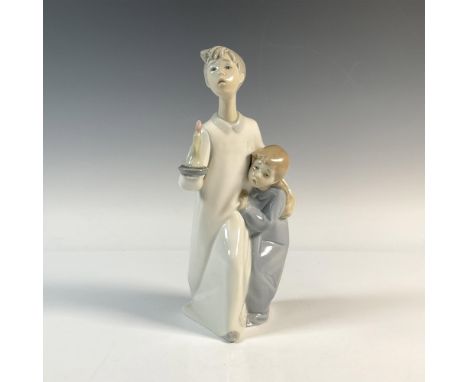 A figurine of a young boy, gently guiding his sister forward in a white robe illuminated by a lit candle, as she clings to hi