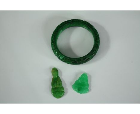 A small collection of jade consisting of a bangle and two seated Buddha figures. The bangle is etched with a delicate floral 