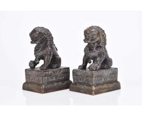 A pair of Chinese bronze guardian lionsModelled in typical seated pose, the male with his front paw resting on an embroidered