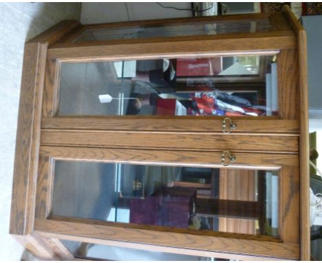 A modern light oak display cabinet, having angled sides, enclosed by a pair of glazed panelled doors, on a plinth  36''h  40'