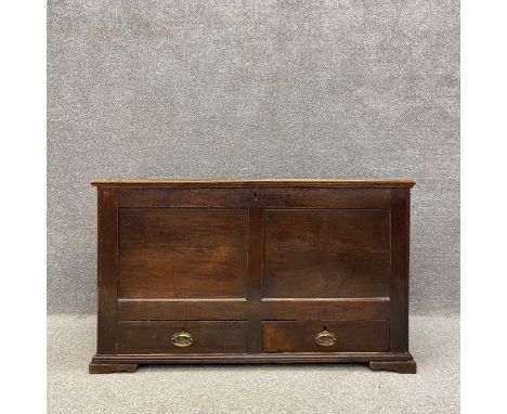 A Georgian oak mule chest having a two plank hinged top over a panelled trunk above two lower drawers mounted with oval brass