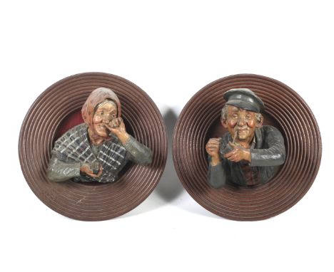 A pair of Austrian terracotta wall plaques. Modelled as a man smoking a pipe and a woman using a snuff box, mounted on ribbed