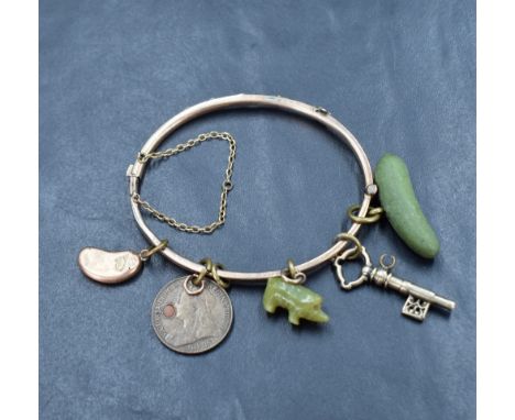 A vintage yellow metal hinged bangle of slim buckled belt form having five attached charms including coin, key, polished ston