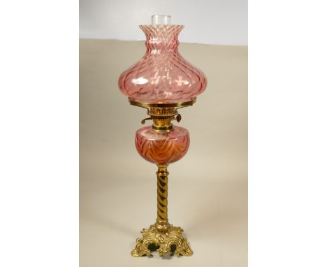 A brass oil lamp with Cranberry fluted shade &amp; reservoir on cast barley twist column, 67cm.