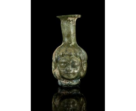 Ca. 100-300 ADAn ancient flask blown from two parts of olive green clear glass with a Janus head of a youth. The young boy wi