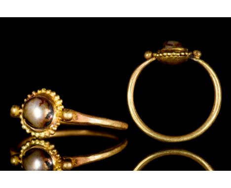 Ca. 600 ADA gold finger ring comprised of a thin round hoop with faceted shoulders and an applied circular bezel with a pearl