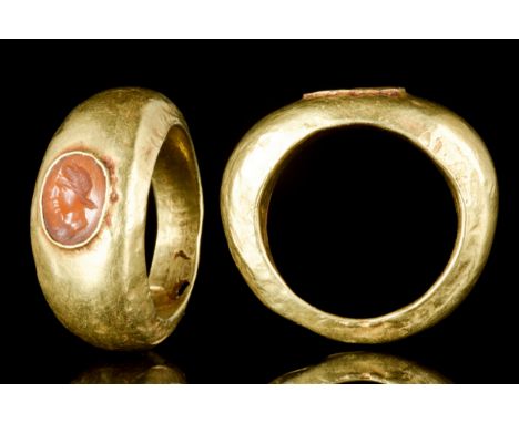 Ca. 100-300 ADA gold finger ring of a broad hoop with faceted edges featuring a carnelian stone intaglio finely carved with t