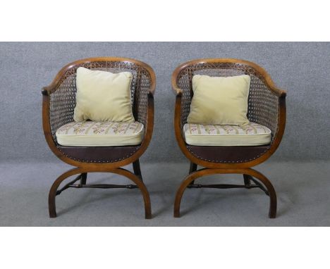 A pair of early 20th century mahogany bergere tub armchairs with fitted tapestry upholstered seats on X frame supports. 