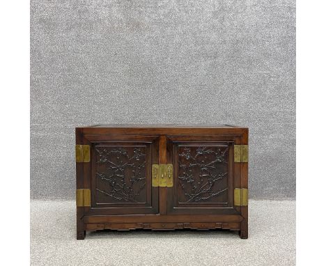 A 20th century Chinese hardwood cabinet with a traditional brass lock and hinges having panelled doors and sides carved with 