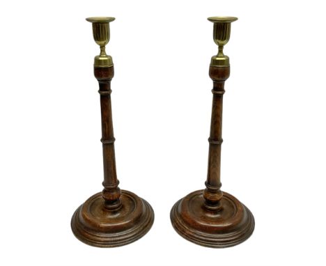 Pair of George III style oak candlesticks, each with fluted brass socket with removable brass nozzle, upon a tapering column 