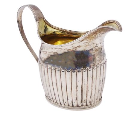 Large George III silver cream jug, of part fluted oval-helmet form, with engraved crest beneath lip, curved handle, and gilt 