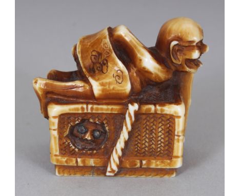 A SIGNED JAPANESE MEIJI PERIOD STAINED IVORY NETSUKE OF AN ONI CATCHER, lying atop a box from the side of which peers out a f