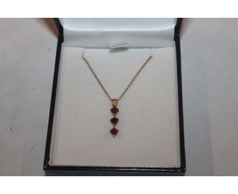 A yellow metal pendant marked 10K, set with ruby coloured stones hung to a fine link chain