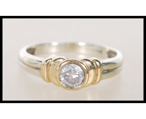 A 9ct two tone gold diamond solitaire ring having a bezel set brilliant cut diamond on a reeded white gold shank with yellow 