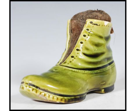 A 19th Century Victorian ceramic pin cushion in the form of boot having a green glaze with a straw pin cushion to the interio