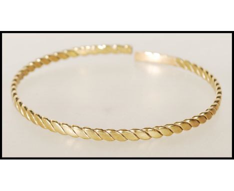 A 20th century stamped 9ct yellow gold bangle bracelet of twisted form, having an opening to the back. Weight 13.1g.&nbsp;