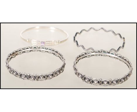 A group of four silver bangle bracelets to include a stamped 925 wave design bangle, a stamped 925 bangle with a pierced geom