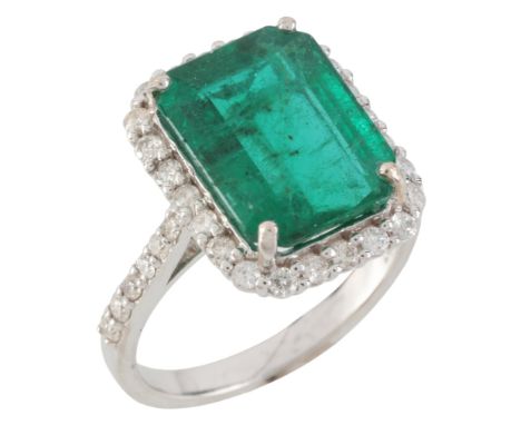 AN EMERALD AND DIAMOND CLUSTER RINGin 18ct white gold, set with a step cut emerald of c.5.00 carats, surrounded by a border o