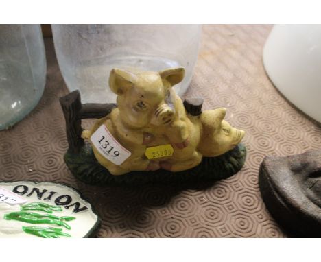A cast iron painted door stop in the form of pigs at a gate 