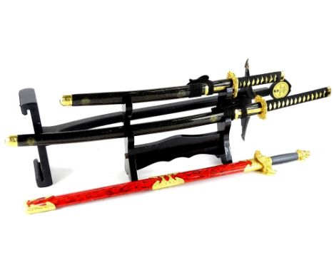 Three replica Samurai swords, each in decorative scabbard with gilt coloured metal mounts and two stands.