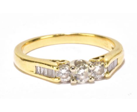 A yellow metal diamond ring with three round brilliant cut stones and ten baguette cut stones to the shoulders, size K, appro