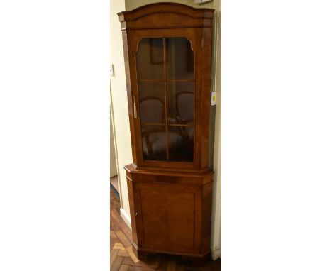 A reproduction burr walnut veneered free standing corner cabinet, the single glazed door enclosing two fixed shelves, above b