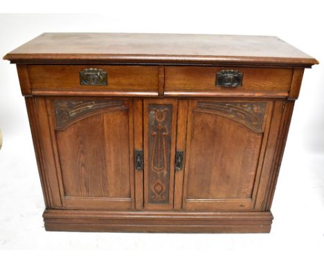 An Arts and Crafts style oak sideboard with two frieze drawers above central carved panel flanked by two panelled doors, rais