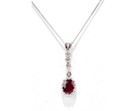 A 9ct white gold ruby and diamond pendant suspended on a fine link 9ct white gold chain, the oval ruby set beneath three tiny
