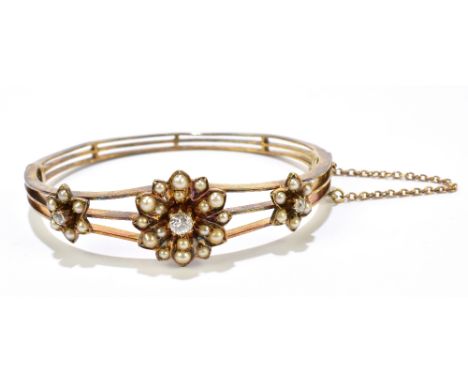 A 15ct yellow gold, seed pearl and diamond set hinged snap bangle of openwork design, the central flower head set with a diam