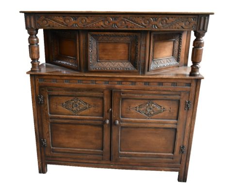 A reproduction oak court cupboard with carved detail, the hinged door to upper section enclosing single shelf above twin pane