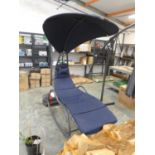 Grey aluminium framed outdoor garden sun lounger with upholstered blue cushions and overhead shade