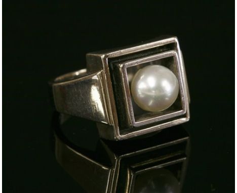 A white gold Art Deco-style single stone cultured pearl ring, with a 6.6mm cultured pearl, peg set to two square frames, with