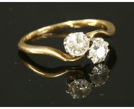 A two stone diamond crossover ring, with two old brilliant cut diamonds, claw set to white rex collets. Yellow underbezels, w