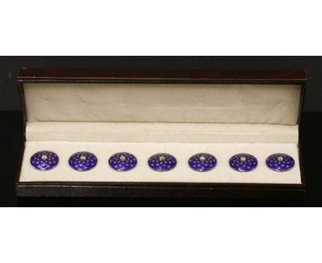 A cased gold and silver set of seven blue enamel dress buttons, of shallow domed circular form. A brilliant cut diamond, rub 