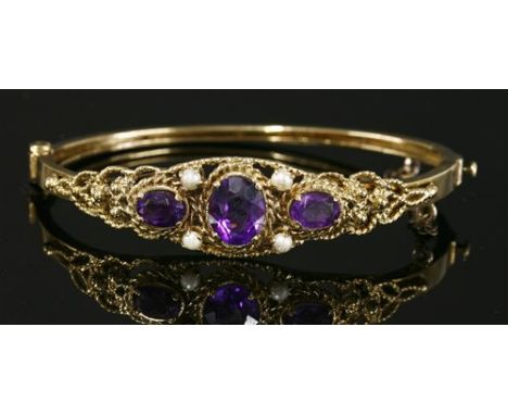 A Victorian-style amethyst and split pearl hinged bangle, with three oval graduated mixed cut amethysts, claw set between pai