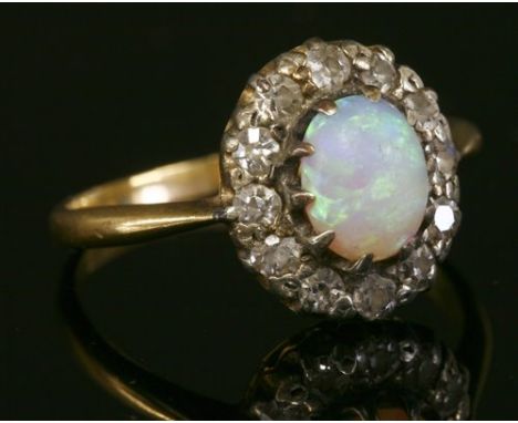 A gold opal and diamond cluster ring, with an oval cabochon opal, claw set to a border of eight cut diamonds, all set in whit