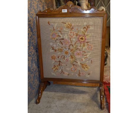 A reproduction walnut fire screen with wool work panel and knee carved cabriole supports.