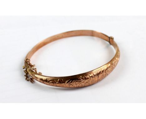 A 9ct rose gold foliate scroll and floral engraved hollow snap bangle with safety chain, aperture 6 x 5cm, approx 5.7g.