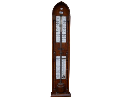 An Edwardian oak lancet topped barometer, with four white enamel plaques set with various gauges, thermometer and details, in
