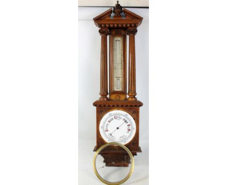 An Edwardian carved oak wheel barometer with thermometer flanked by fluted columns above circular dial within a foliate detai