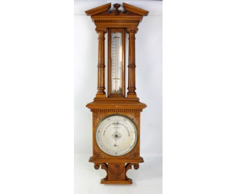 An Edwardian carved oak wheel barometer with thermometer flanked by fluted pillars above the silvered dial inscribed 'M Arons