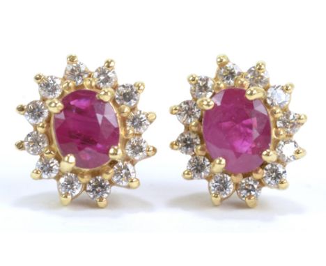 A pair of yellow metal and ruby ear studs, the oval cut stones combined approx 1ct, each within border of twelve cubic zircon