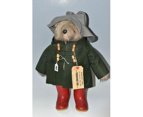 A GABRIELLE DESIGNS PADDINGTON BEAR, green duffel coat, faded blue hat and red Dunlop Wellingtons, right eye has come loose a