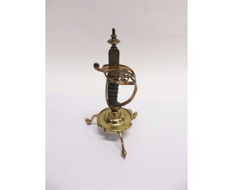 A VICTORIAN BRASS SWORD HILT CANDLESTICK  with a fish-skin grip, on tripod spur supports, 29cm high (lacking sconce).
