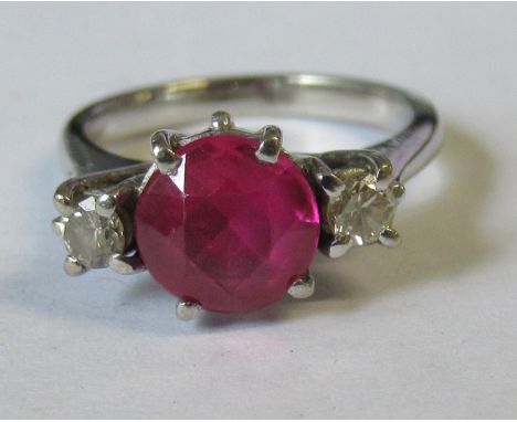 A ruby and diamond ring, set in white metal, the central round cut ruby, possibly a synthetic flanked by diamonds, approx. 0.