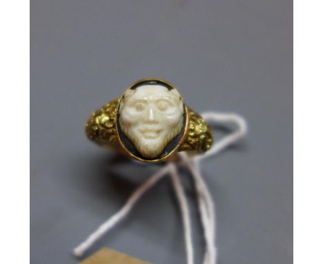 A yellow metal signet ring, having a bone carving of a demon on an onyx mount, the ring with floral engraving 