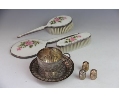 An Indian white metal tea cup and saucer, decorated throughout with foliate motifs, a white metal and enamel three piece dres