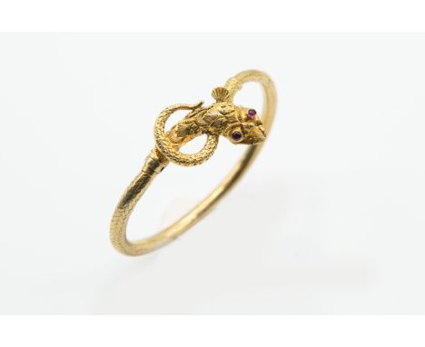 A VICTORIAN SNAKE BANGLE, the realistically moulded snake head with elaborate engraved detailing set with two ruby highlights